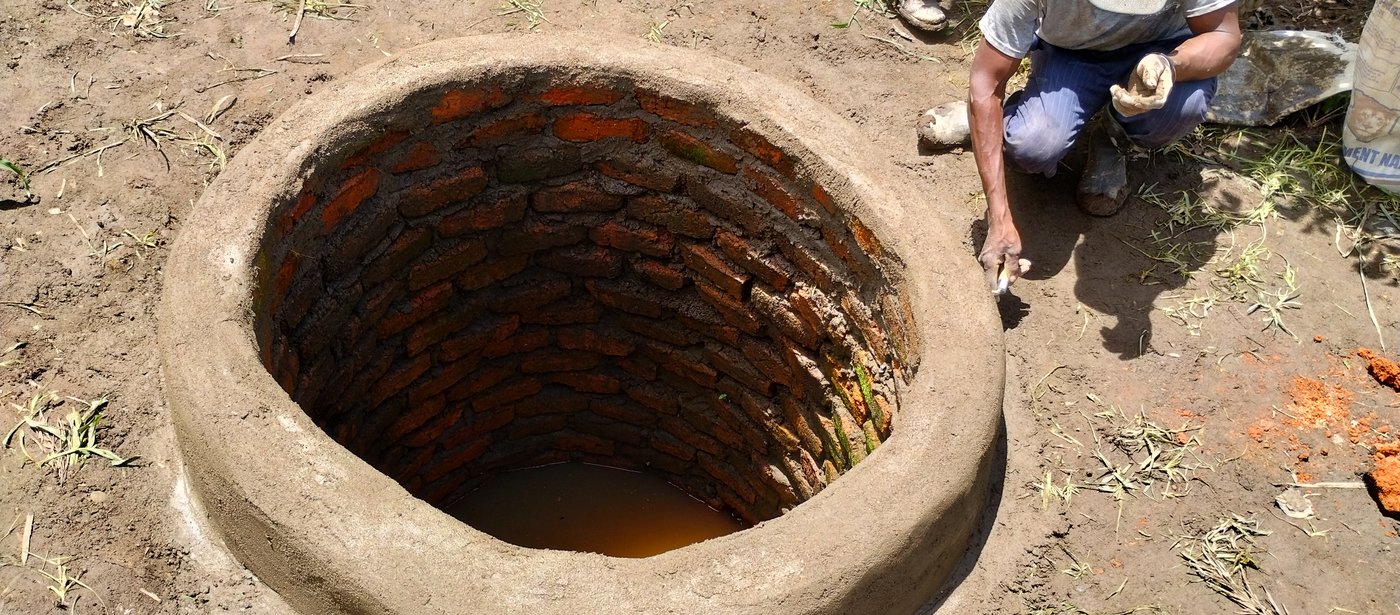 A hand-dug well lined with brick, a mason finishing the concrete collar