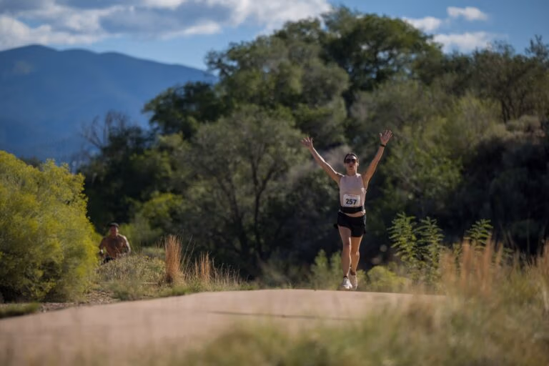 A runner with both arms raised in celebration on the trail