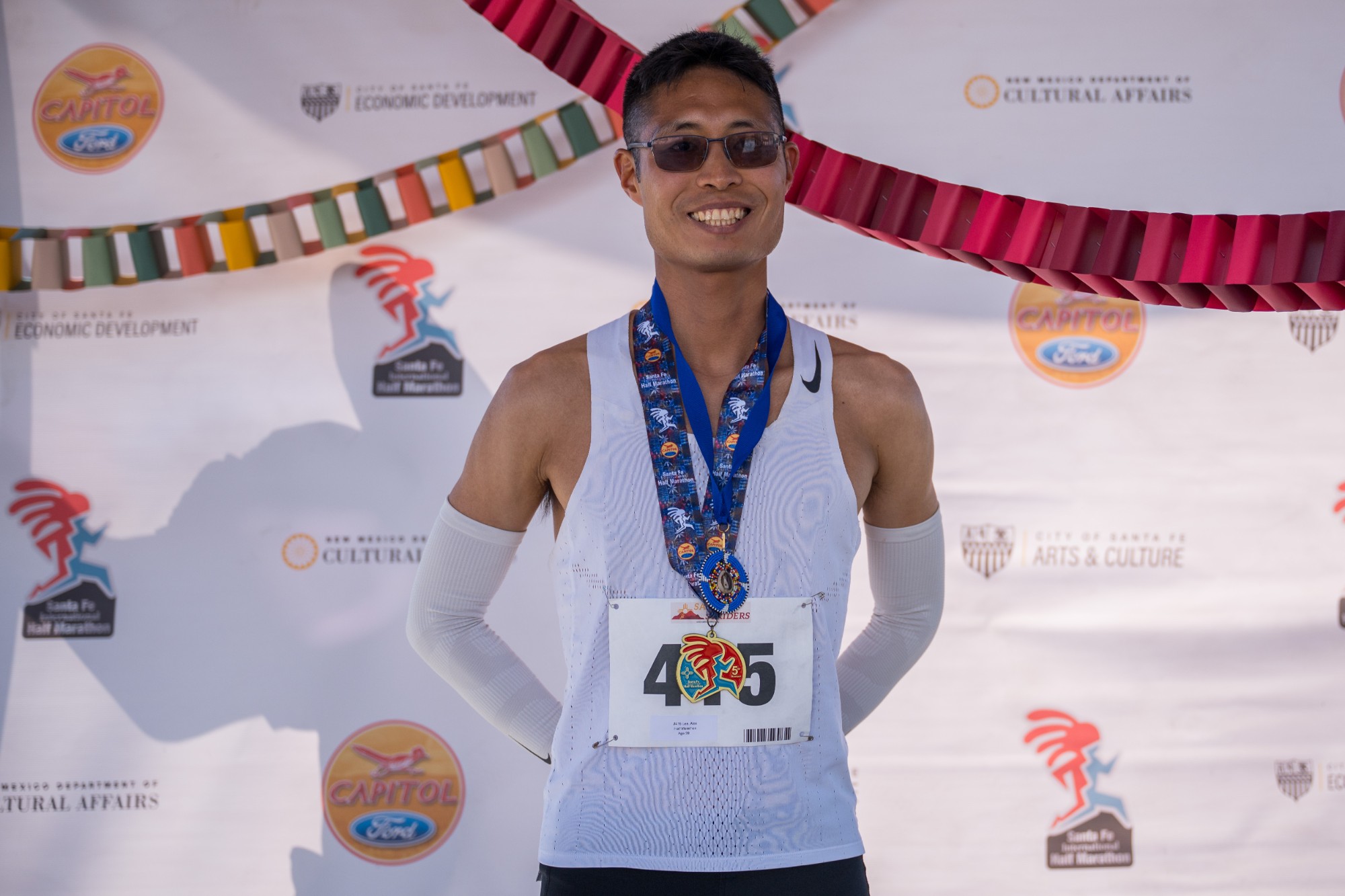 Overall winner Alex Lee smiling with his finisher medal in front of the race backdrop
