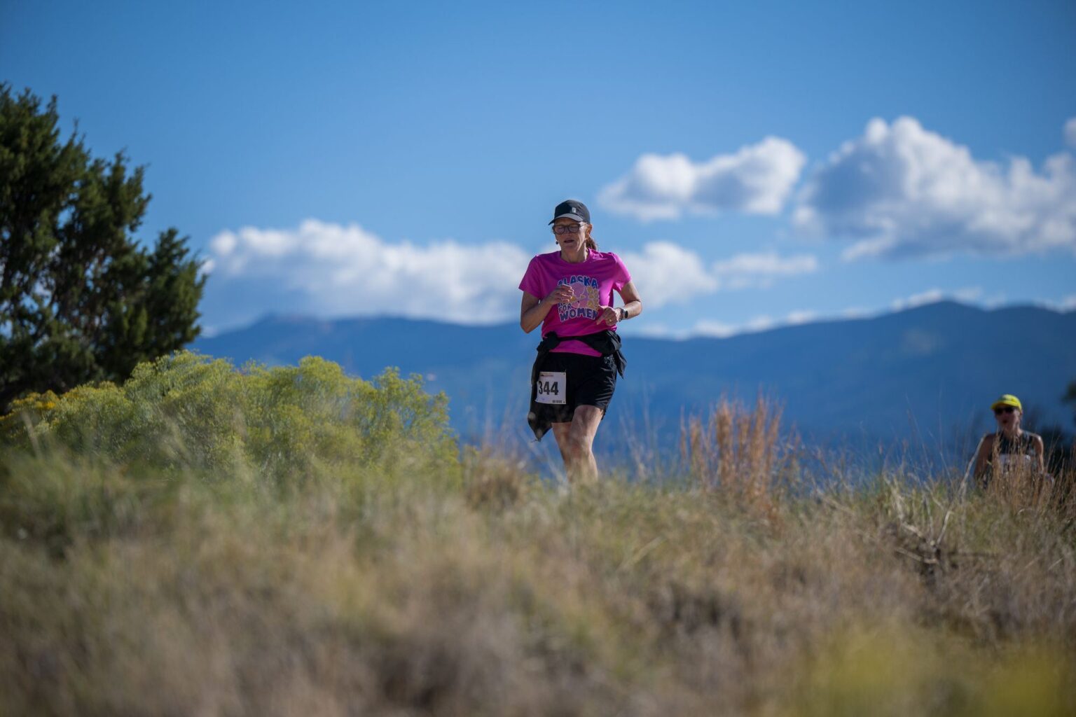 A runner in pink against blue sky and distant mountains