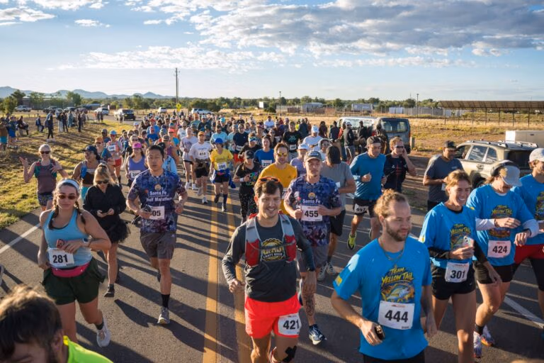 A smiling crowd of runners surging toward the camera at the start of the 2026 race