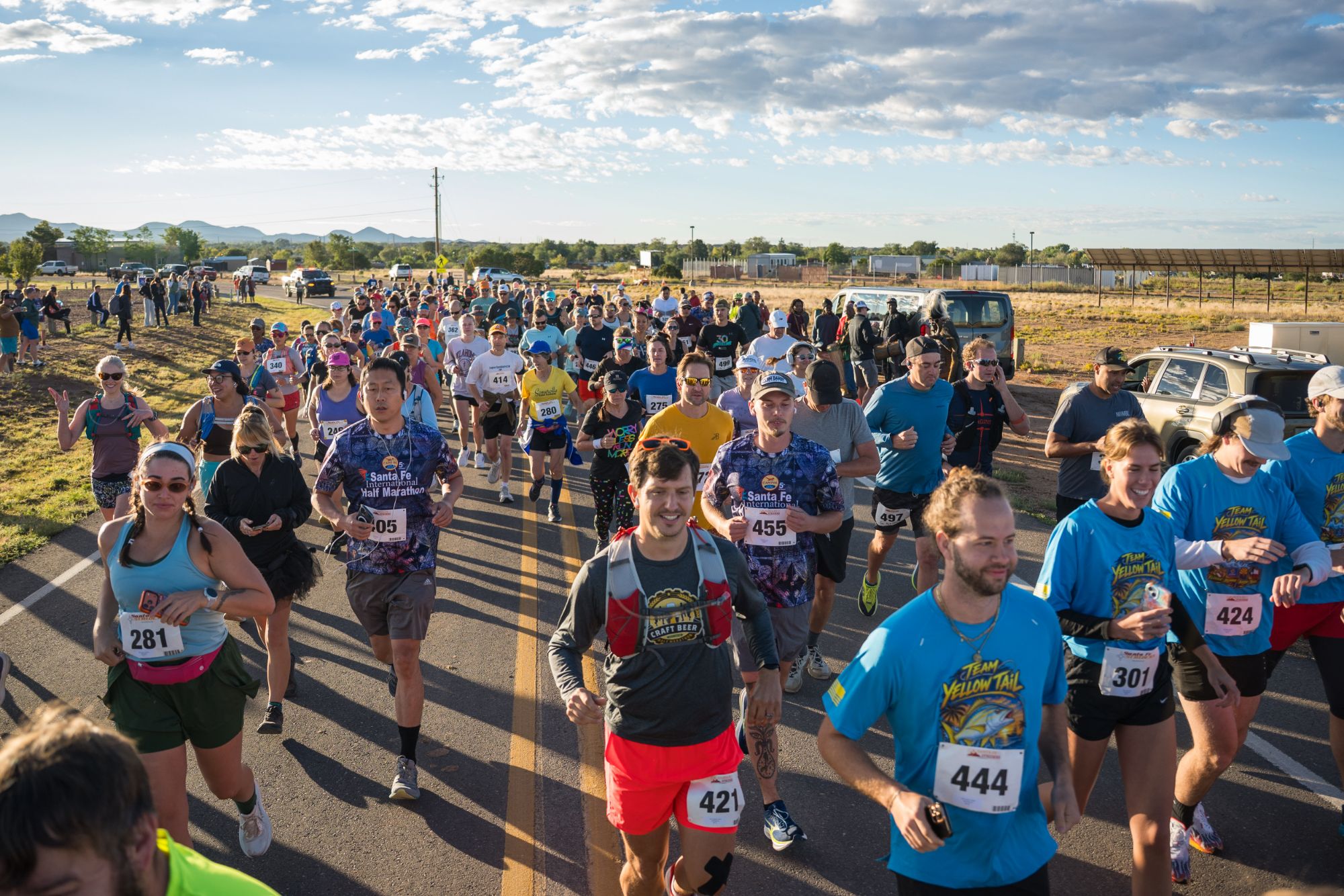 A smiling crowd of runners surging toward the camera at the start of the 2026 Santa Fe International Half Marathon