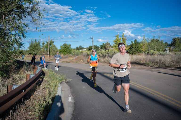 Half marathon runners round a bend in the road under a bright blue Santa Fe sky
